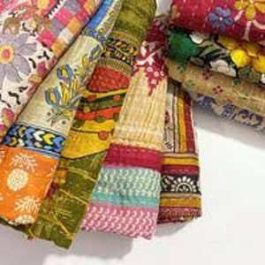 Op de afbeelding: Een verzameling kleurrijke, bedrukte stoffen, mogelijk quilts of textiel, met een verscheidenheid aan ontwerpen, waaronder bloemen, geometrische en abstracte patronen. De stoffen tonen een mix van kleuren zoals oranje, geel, groen en roze.