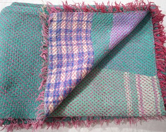 May include: A green and purple kantha quilt with a pink fringe. The quilt is made of recycled saris and is hand-stitched.