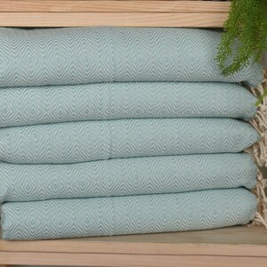 May include: A stack of five light blue towels with a diamond pattern. The towels are folded and stacked on a wooden shelf.
