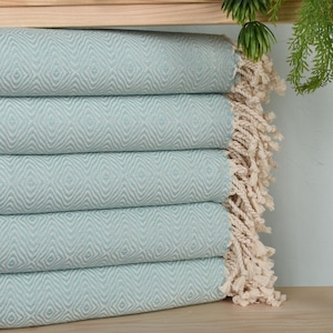 May include: A stack of five light blue throw blankets with a diamond pattern and white fringe.