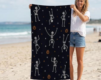 May include: A rectangular beach towel featuring a dark navy blue background with a repeating pattern of white skeletons in various dancing poses, orange jack-o'-lantern pumpkins, and small white and orange four-pointed stars scattered throughout.