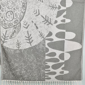 Może przedstawiać: Szary i biały wzorzysty ręcznik plażowy ze stylizowanym wzorem żółwia i frędzlami.