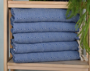Op de afbeelding: Een stapel blauwe en witte handdoeken met franjes aan de randen. De handdoeken zijn gevouwen en gestapeld op een houten plank.