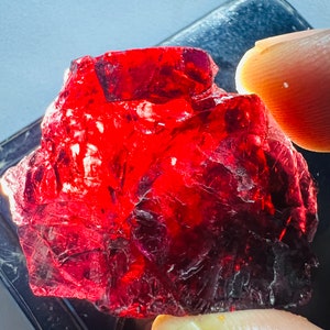 Puede incluir: Una gran gema roja facetada con una forma irregular y áspera. La gema es translúcida y tiene un color rojo intenso.