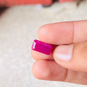 Puede incluir: Una gema rosa vibrante con forma rectangular y corte facetado.