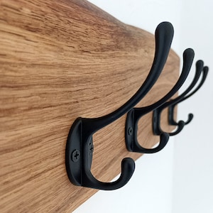 May include: A wooden wall-mounted coat rack with four black metal hooks. The wood has a natural grain pattern.