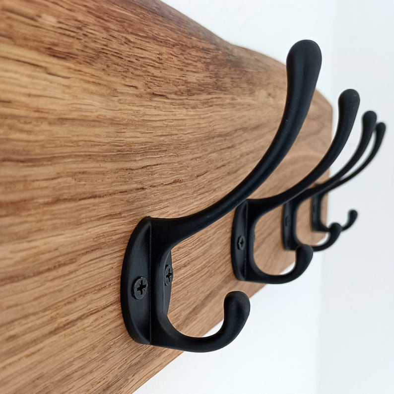 May include: A wooden wall-mounted coat rack with four black metal hooks. The wood has a natural grain pattern.
