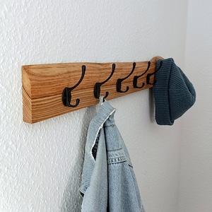 May include: A wooden coat rack with six black metal hooks. A blue denim jacket and a dark blue beanie are hanging on the hooks.