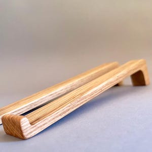 May include: Two wooden cabinet pulls with a natural wood grain finish. The pulls have a rectangular shape with a curved handle, and are designed for easy gripping. The pulls are made of light-colored wood.