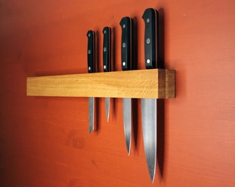 Peut inclure: Cinq couteaux de cuisine avec des manches noirs sont montés sur une bande magnétique en bois. Les couteaux sont disposés en rangée, le plus grand couteau à droite et le plus petit couteau à gauche.
