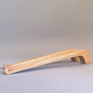 May include: A light-colored wooden laptop stand with a sloped design. The stand has a rectangular base and a curved support at the back. The wood grain is visible, and the stand is designed to elevate a laptop for ergonomic use.