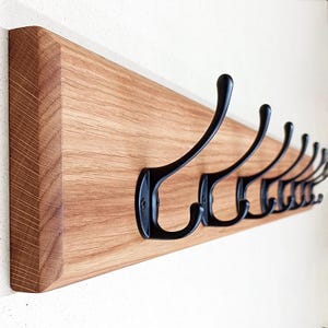 Könnte beinhalten: Ein Holz-Kleiderständer mit acht schwarzen Metallhaken. Der Ständer ist aus hellbraunem Holz und hat eine natürliche Oberfläche.