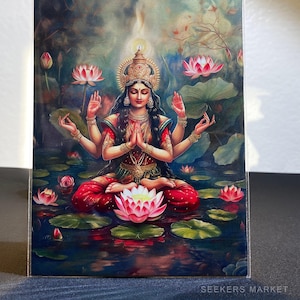 Puede incluir: Una pintura de una diosa hindú con cuatro brazos, sentada en posición de loto sobre un lecho de nenúfares. Lleva un sari rojo y dorado y tiene una expresión serena en su rostro. El fondo es un exuberante bosque verde con un cielo azul.