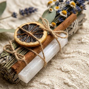 May include: A bundle of sage, cinnamon sticks, and a selenite wand tied with twine. A dried orange slice and sprigs of lavender and chamomile are included. The items are arranged on a textured, off-white surface.