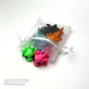 May include: A set of five small, colourful axolotl figurines in a white organza bag. The axolotls are green, pink, blue, orange, and black.