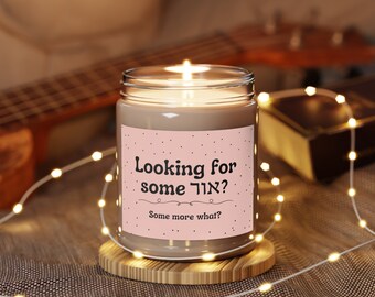 May include: A brown candle with a pink label that says "Looking for some  אוד?" and "Some more what?" The candle is lit and sitting on a wooden coaster.