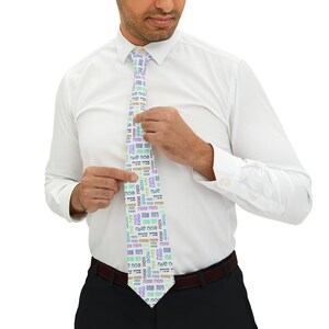 May include: A white tie with a colorful pattern of Hebrew text that says "Happy Passover" in Hebrew. The tie is being worn by a person.