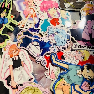 May include: A collection of colorful anime-style stickers featuring various characters. The stickers showcase a range of designs, including figures with pink, blue, and blonde hair, and some with angel wings. Some stickers have text like "Sweet dreams" and "calico critters".