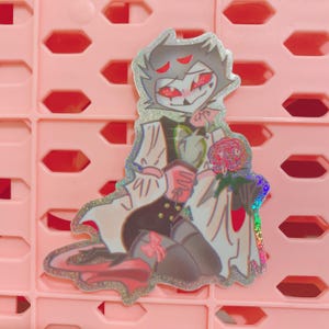 May include: Holographic sticker featuring a cartoon character with gray hair, red eyes, and a black and white outfit. The character is holding a red rose and has a mischievous expression. The sticker has a glittery, iridescent border.
