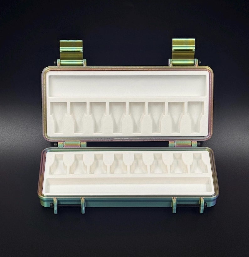 Puede incluir: Un estuche de almacenamiento rectangular de metal iridiscente con dos bisagras y cierres resistentes. El interior cuenta con una inserci&oacute;n de espuma blanca con ocho ranuras moldeadas para objetos peque&ntilde;os y un compartimento estrecho.