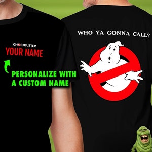 May include: Black t-shirt with a white Ghostbusters logo on the back. The logo features a ghost with the words "Who ya gonna call?" above it. The front of the shirt has the words "Ghostbuster" and "Your Name" in white text.
