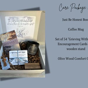 May include: A care package containing a black coffee mug, a book titled "Just Be Honest", a set of 54 encouragement cards with a wooden stand, and a small olive wood cross. The package is presented in a white box with brown packing paper.