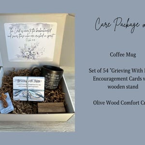 May include: A white gift box filled with brown paper. The box contains a black coffee mug, a set of 54 "Grieving With Faith" encouragement cards with a wooden stand, and a small olive wood comfort cross. The box lid has a card with a floral design and the text "The Lord is near to the brokenhearted and saves those who are crushed in spirit - Psalm 34:18"