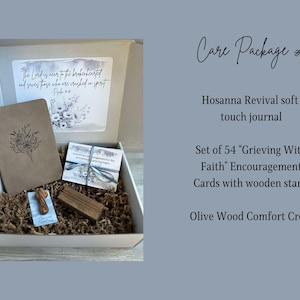 May include: A white gift box filled with a brown journal, a set of 54 encouragement cards, a wooden stand, and a small olive wood cross. The box lid has a floral design and the text "The Lord is near to the brokenhearted and saves those who are crushed in spirit."  Psalm 34:18