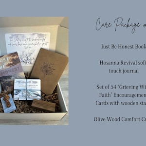 May include: A care package containing a brown box filled with items including a book titled "Just Be Honest", a soft touch journal, a set of 54 encouragement cards with a wooden stand, and a wooden cross. The box is decorated with a scripture verse.