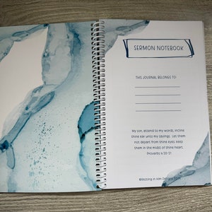 Peut inclure: Un carnet &agrave; spirales bleu et blanc avec le titre "Sermon Notebook" et le texte "Ce journal appartient &agrave;" suivi d'une ligne vide. Le carnet a un design aquarelle sur la couverture.