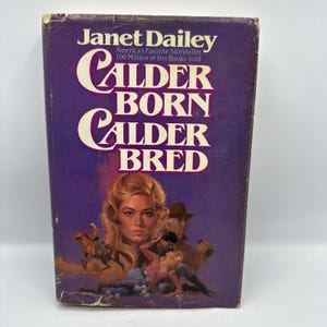 May include: A vintage paperback book titled "Calder Born, Calder Bred" by Janet Dailey. The cover is a deep purple with white lettering and a portrait of a woman with long blonde hair. The cover also features illustrations of cowboys and a woman.
