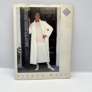 May include: A magazine cover featuring a woman in a white coat, pink sweater, and white pleated skirt. The text "EILEEN WEST" is at the bottom. The woman is standing in a doorway. The background is a blurred outdoor scene.