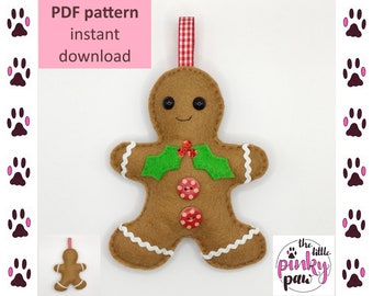 May include: A felt gingerbread man ornament with a red and white gingham ribbon, green holly leaves, and red buttons. The ornament is brown with white icing details. The text "the little pinky paw" is visible in the bottom right corner of the image.