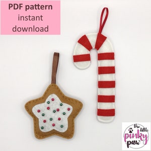 Puede incluir: Patrón PDF para dos adornos navideños de fieltro: una estrella de jengibre con glaseado blanco y chispas rojas y verdes, y un bastón de caramelo con rayas rojas y blancas. Los adornos cuelgan de cuerdas marrones y blancas. El texto "The Little Pinky Paw" está en la esquina inferior derecha.