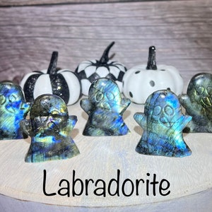 May include: Five iridescent blue and green labradorite ghost figurines on a wooden surface. The text "Labradorite" is written below the figurines.