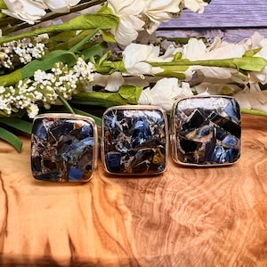 May include: Three square-shaped rings with a mosaic of blue, brown, and black stones set in silver.