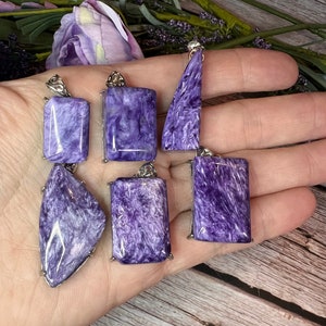 May include: Six purple and silver pendant charms made of labradorite gemstone. The charms are in various shapes, including rectangular and triangular.