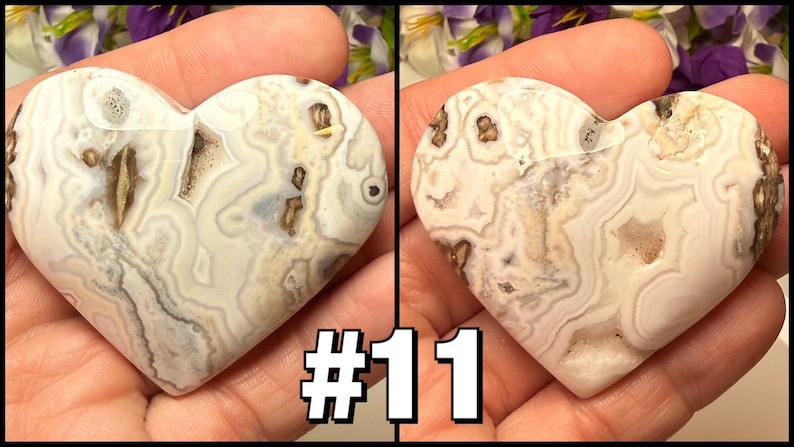 May include: Two heart-shaped stones with a swirling pattern of white, gray, and brown. The stones are held in a hand, and the number "#11" is displayed in the lower right corner. The stones have a polished surface.