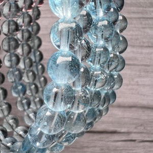 May include: A close-up of a light blue gemstone bracelet with round beads. The beads are translucent and have a slight sparkle.