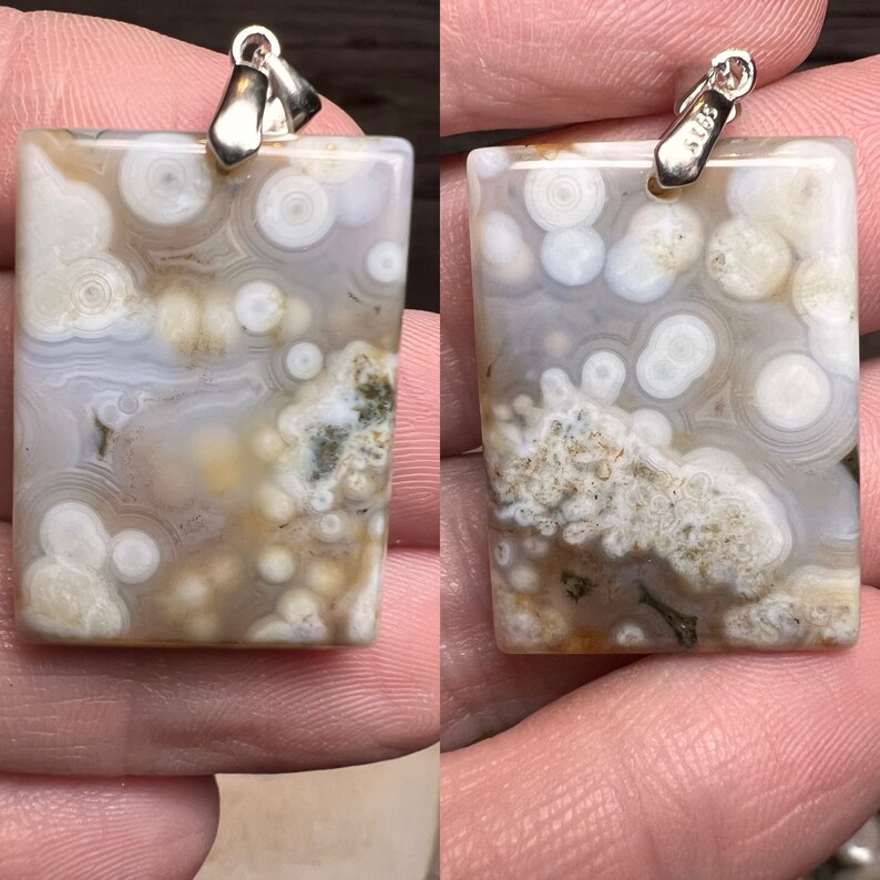 Puede incluir: Un colgante de &aacute;gata blanca con una argolla de plata. La &aacute;gata tiene un patr&oacute;n de remolino de blanco y marr&oacute;n con peque&ntilde;os c&iacute;rculos blancos en todo.