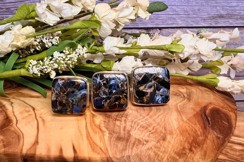 May include: Three square-shaped rings with a mosaic of blue, brown, and black stones set in silver.