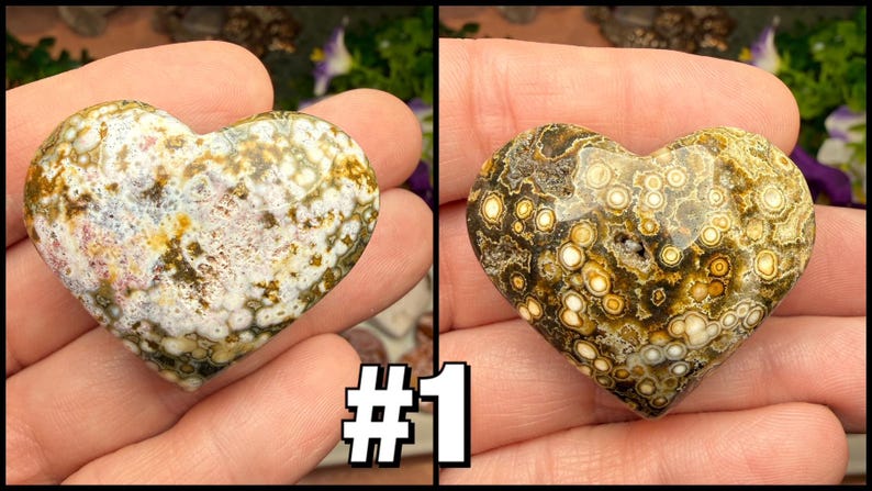 May include: Two heart-shaped stones with unique patterns. One features a mix of white, green, and brown hues, while the other displays a pattern of brown and yellow circles. The stones are held in a hand.