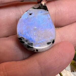 May include: A teardrop-shaped iridescent moonstone pendant with black inclusions. The pendant is set in silver and has a polished finish.