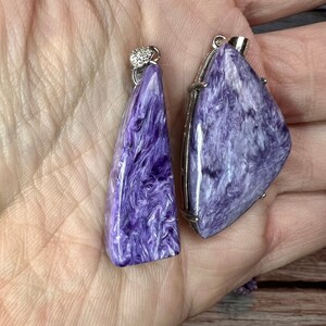 May include: Two purple and white gemstone pendants with silver settings. The pendants are shaped like triangles and have a swirling pattern.