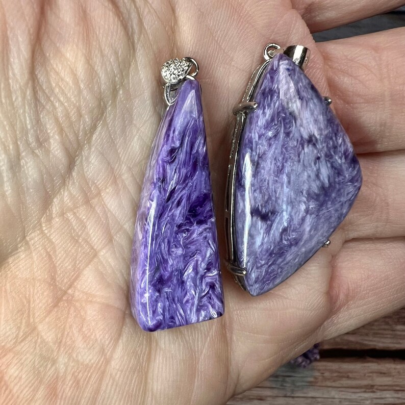 May include: Two purple and white gemstone pendants with silver settings. The pendants are shaped like triangles and have a swirling pattern.
