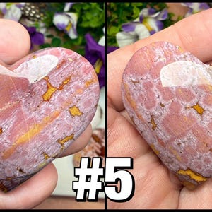 May include: Two heart-shaped stones with a pink and gold pattern. The stones are held in a hand. The stones have a white area at the top. The number "5" is in the lower right corner.