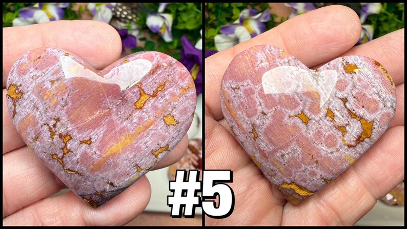 May include: Two heart-shaped stones with a pink and gold pattern. The stones are held in a hand. The stones have a white area at the top. The number "5" is in the lower right corner.
