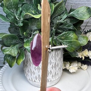 Op de afbeelding: Een houten stok met een ovaalvormig stuk hars in paars en wit dat eraan is bevestigd. De stok wordt gebruikt om het harsstuk vast te houden.