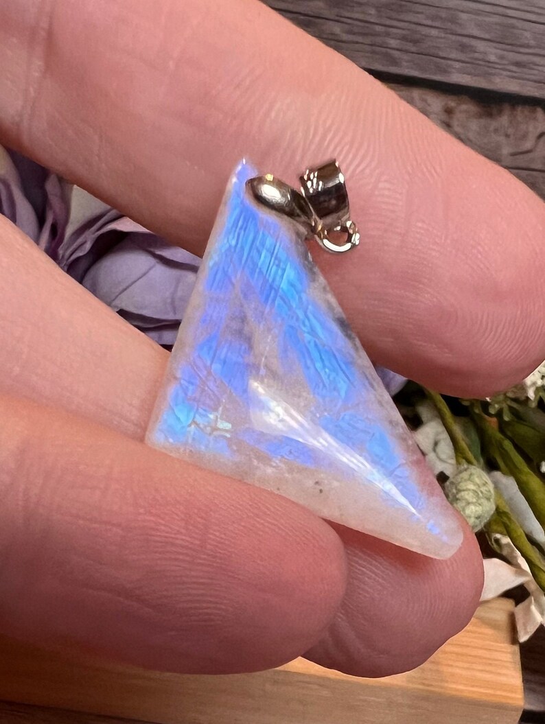 May include: A triangular iridescent moonstone pendant with a silver bail. The stone has a white base with blue and purple iridescent flashes.