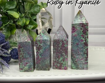 May include: Four Ruby in Kyanite crystal towers. The crystals are a mix of deep red, green, and gray. The crystals are displayed on a white tray. The text "Ruby in Kyanite" is written in cursive at the top of the image.